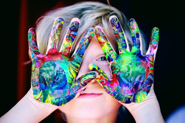 Lille barn der holder hænderne op foran hovedet med farverig maling på hænderne