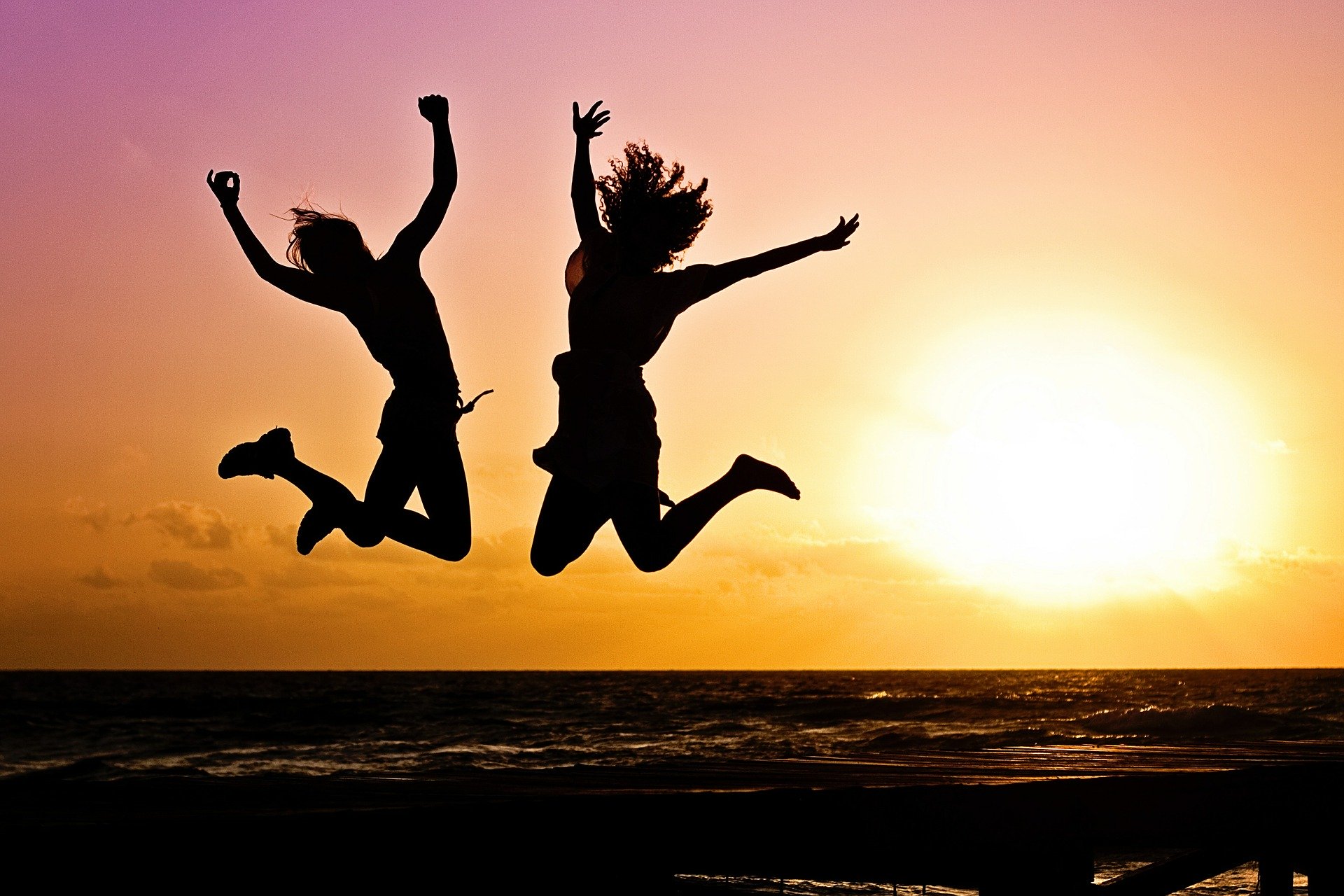 To piger der hopper i solnedgangen med havet i baggrunden